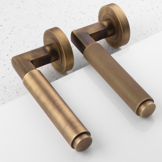 Image showing two door handles on a round rose in an antique brass finish made by Carlisle Brass.  Available to order from Trade Door Handles in Kendal