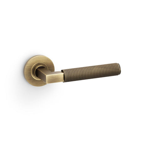 This is an image showing Alexander & Wilks Hurricane Knurled Lever on Round Rose - Antique Brass aw200ab available to order from Trade Door Handles in Kendal, quick delivery and discounted prices.