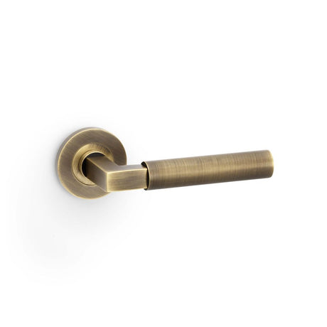 This is an image showing Alexander & Wilks Hurricane Plain Lever on Round Rose - Antique Brass aw201ab available to order from Trade Door Handles in Kendal, quick delivery and discounted prices.