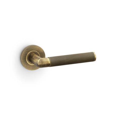 This is an image showing Alexander & Wilks Harrier Knurled Lever on Round Rose - Antique Brass aw210ab available to order from Trade Door Handles in Kendal, quick delivery and discounted prices.
