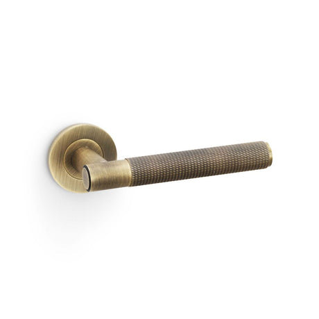 This is an image showing Alexander & Wilks Spitfire Knurled Lever on Round Rose - Antique Brass aw220ab available to order from Trade Door Handles in Kendal, quick delivery and discounted prices.