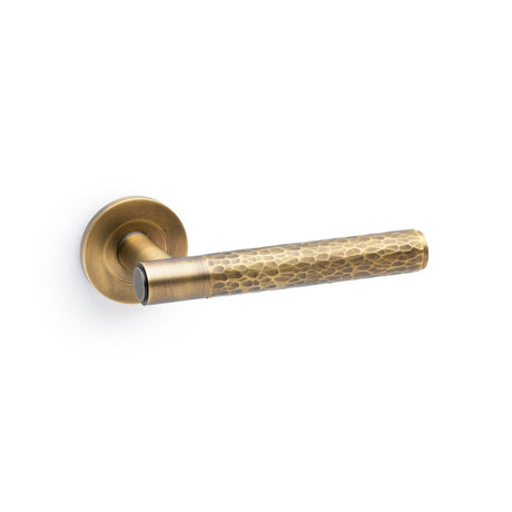 This is an image showing Alexander & Wilks Spitfire Hammered Lever on Round Rose - Italian Brass aw223ib available to order from Trade Door Handles in Kendal, quick delivery and discounted prices.