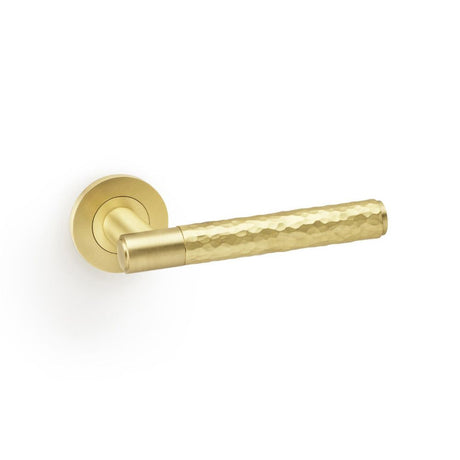 This is an image showing Alexander & Wilks Spitfire Hammered Lever on Round Rose - Satin Brass aw223sb available to order from Trade Door Handles in Kendal, quick delivery and discounted prices.