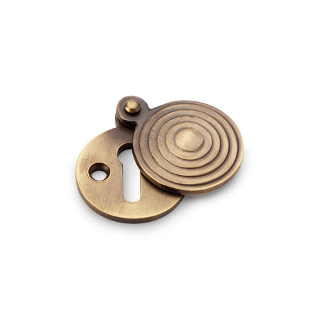 This is an image showing Alexander & Wilks Standard Key Profile Round Escutcheon with Christoph Design Cover - Antique Brass aw382-ab available to order from Trade Door Handles in Kendal, quick delivery and discounted prices.