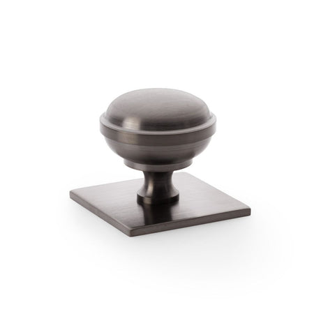 This is an image showing Alexander & Wilks Quantock Cupboard Knob on Square Backplate - Dark Bronze PVD - 38mm aw826-38-dbzpvd available to order from Trade Door Handles in Kendal, quick delivery and discounted prices.