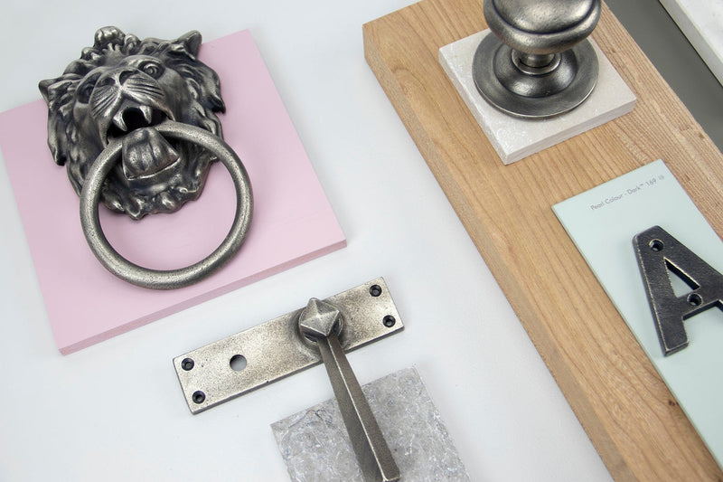 Image showing a range of From The Anvil Antique Pewter Ironmongery including a lions head door knocker, door handle, mortice knobs and a letter A.  All available to order from Trade Door Handles in Kendal