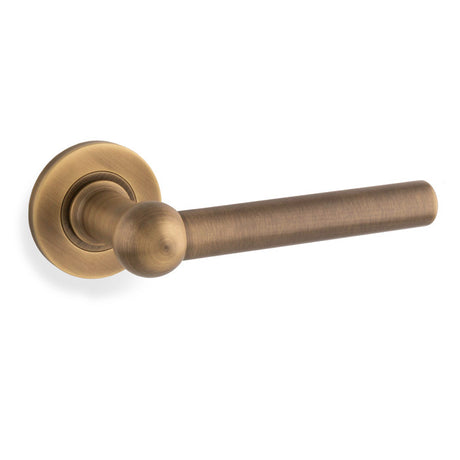 This is an image of Alexander & Wilks - Siskin Lever on Rose - Antique Brass available to order from Trade Door Handles in Kendal, quick delivery and discounted prices.