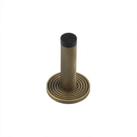 This is an image showing the Frelan - Burlington Knurled Wall Mounted Doorstops Reeded Rose Antique Brass available to order from Trade Door Handles in Kendal