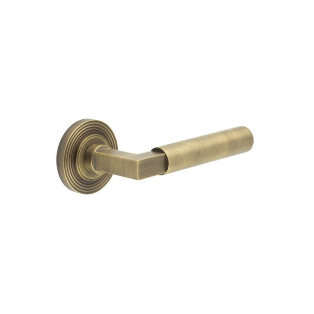 This is an image showing the Frelan - Westminster Door Handle on Reeded Rose Antique Brass available to order from Trade Door Handles in Kendal