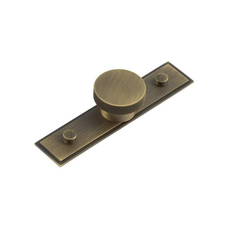 This is an image showing the Frelan - Thaxted Cupboard Knobs 40mm Stepped Backplate Antique Brass available to order from Trade Door Handles in Kendal