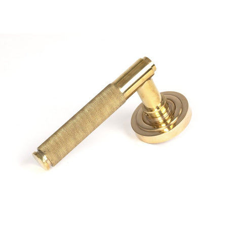 This is an image showing From The Anvil - Polished Brass Brompton Lever on Rose Set (Art Deco) available from trade door handles, quick delivery and discounted prices