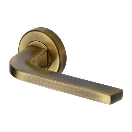 This is a image of a Heritage Brass - Door Handle Lever on Rose Bellagio Design Antique Brass Finish that is available to order from Trade Door Handles in Kendal.