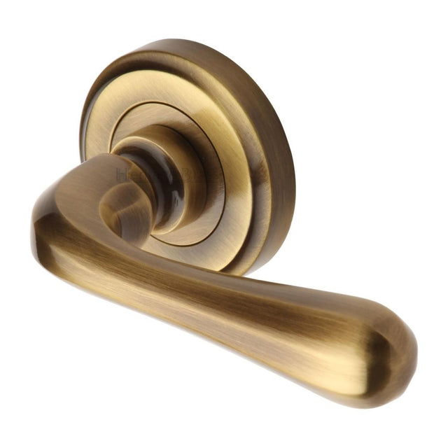 This is an image of a Heritage Brass - Door Handle Lever Latch on Round Rose Charlbury Design Antique Bra, v3020-at that is available to order from Trade Door Handles in Kendal.