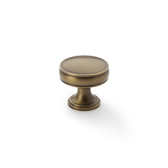 This is an image showing Alexander & Wilks Lynd Cupboard Knob - Antique Brass - 32mm aw808-32-ab available to order from Trade Door Handles in Kendal, quick delivery and discounted prices.