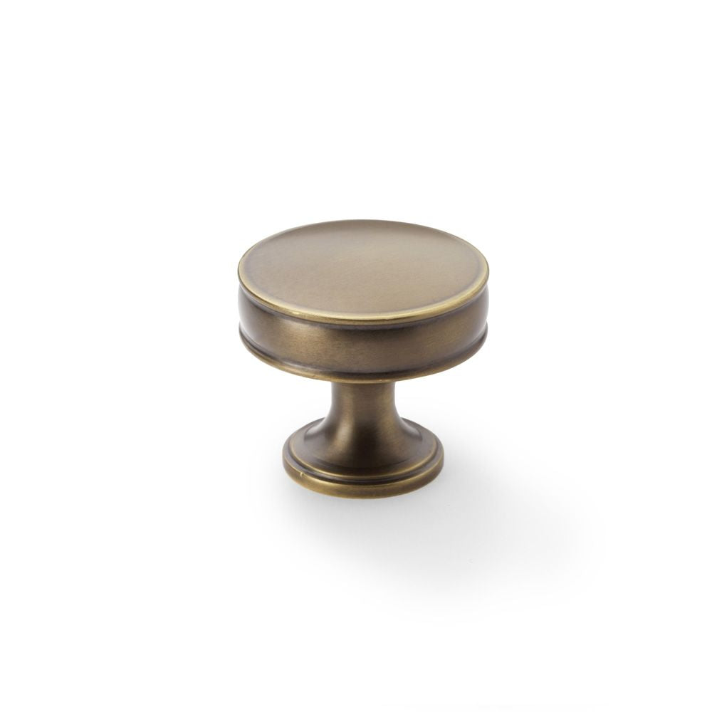 This is an image showing Alexander & Wilks Lynd Cupboard Knob - Antique Brass - 38mm aw808-38-ab available to order from Trade Door Handles in Kendal, quick delivery and discounted prices.