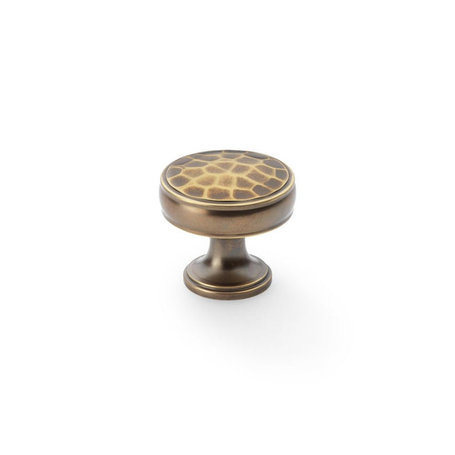 This is an image showing Alexander & Wilks Lynd Hammered Cupboard Knob - Antique Brass - 32mm aw818-32-ab available to order from Trade Door Handles in Kendal, quick delivery and discounted prices.