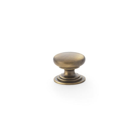 This is an image showing Alexander & Wilks Waltz Round Cupboard Knob on Stepped Rose - Antique Brass - 25mm aw825-25-ab available to order from Trade Door Handles in Kendal, quick delivery and discounted prices.