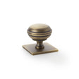 This is an image showing Alexander & Wilks Quantock Cupboard Knob on Square Backplate - Antique Brass - 34mm aw826-34-ab available to order from Trade Door Handles in Kendal, quick delivery and discounted prices.